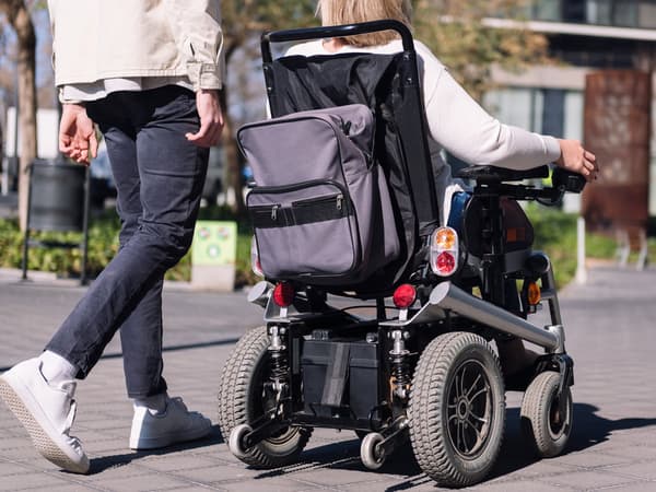 Una persona en cadira de rodes elèctrica passeja amb un amic